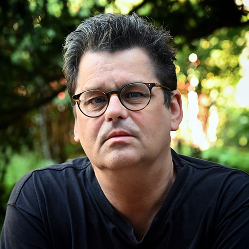 Portrait eines Mannes in der Natur mit dunklen Haaren und Brille.